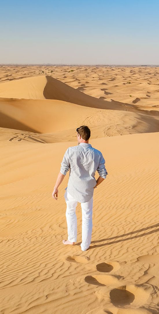 A young man enjoying walking in the red dune during desert safari tour in Dubai